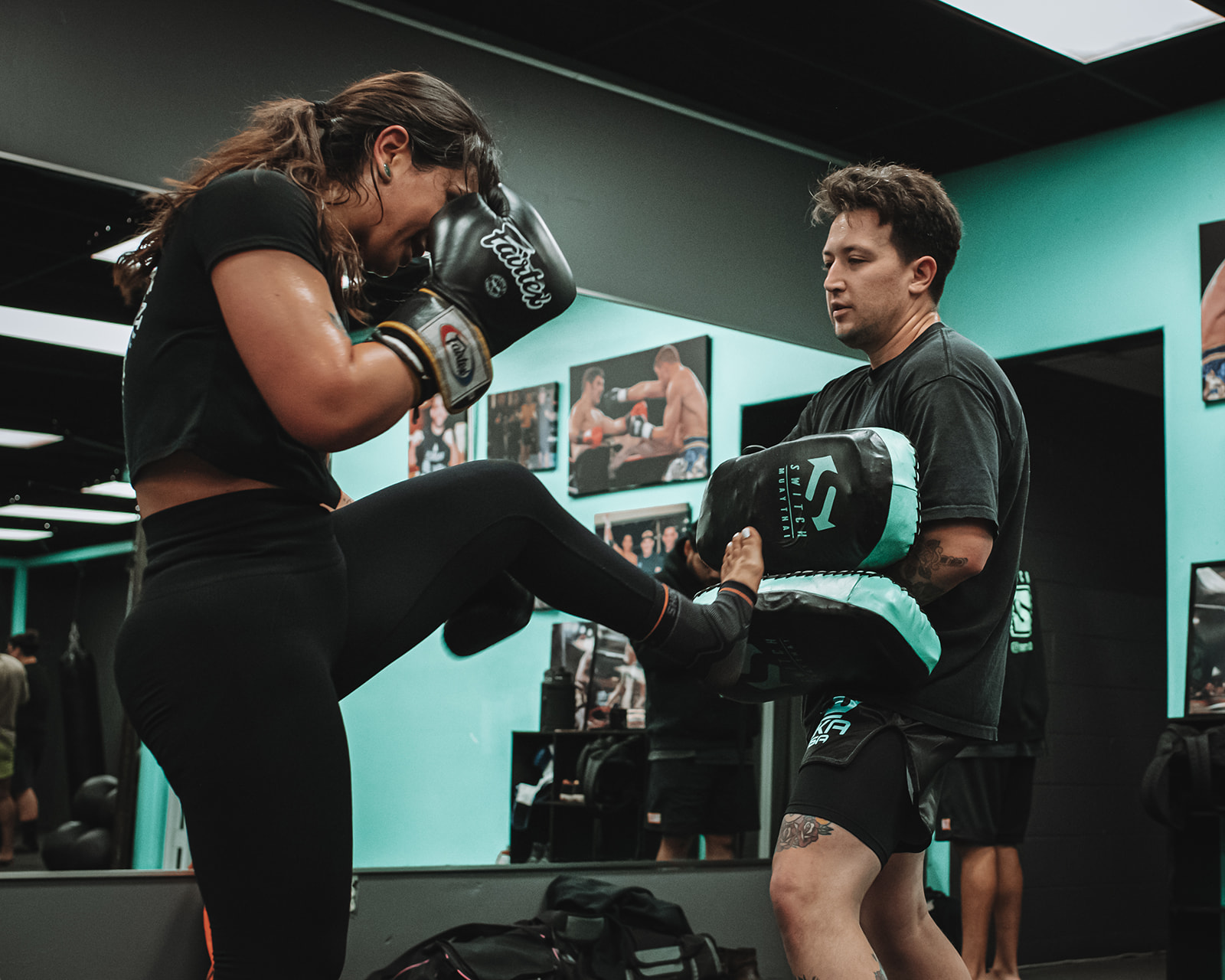 A student throwing a knee into pads held by a coach at Switch Fitness San Diego.