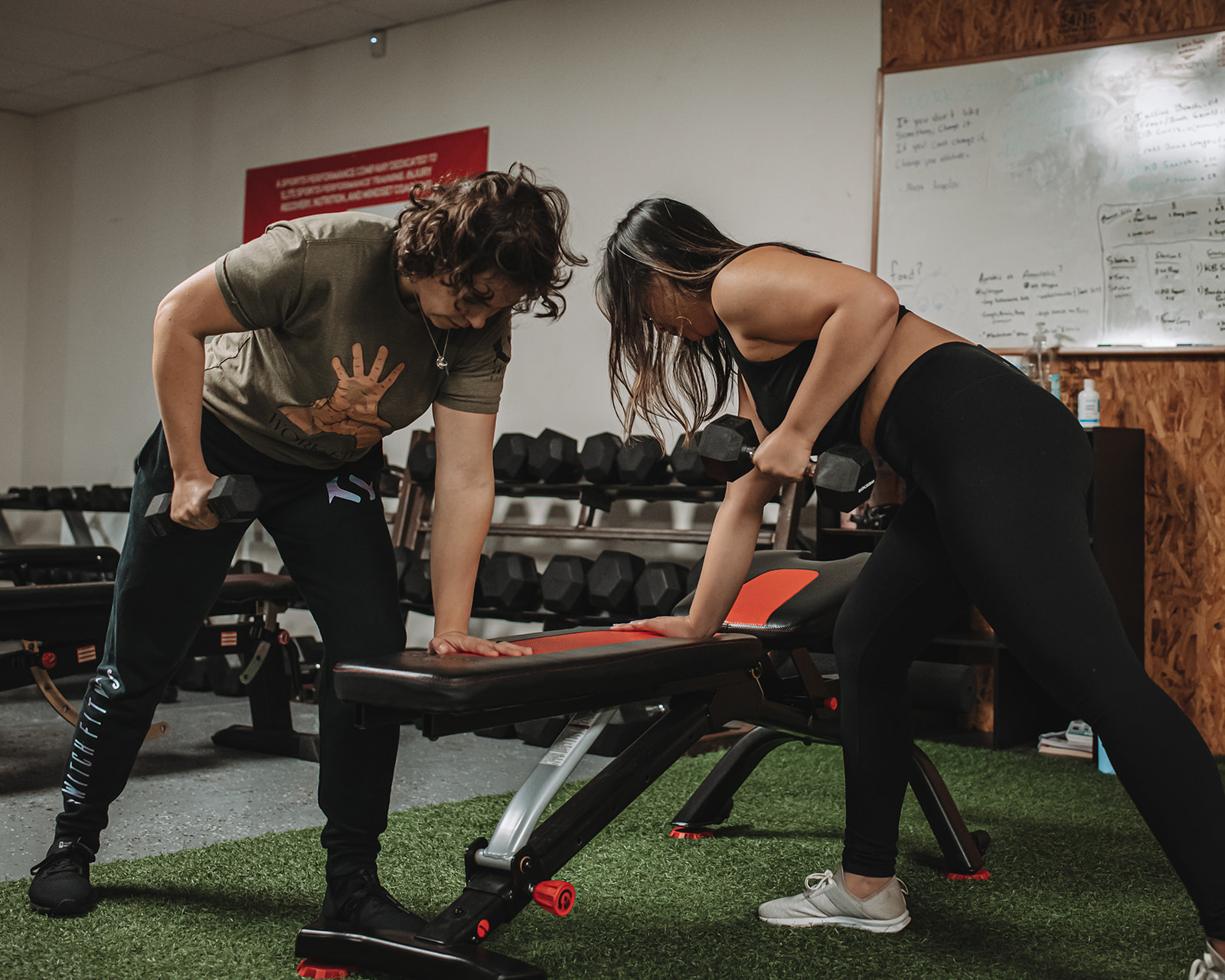 Two members doing dumbbell rows on a bench at Switch Fitness San Diego.